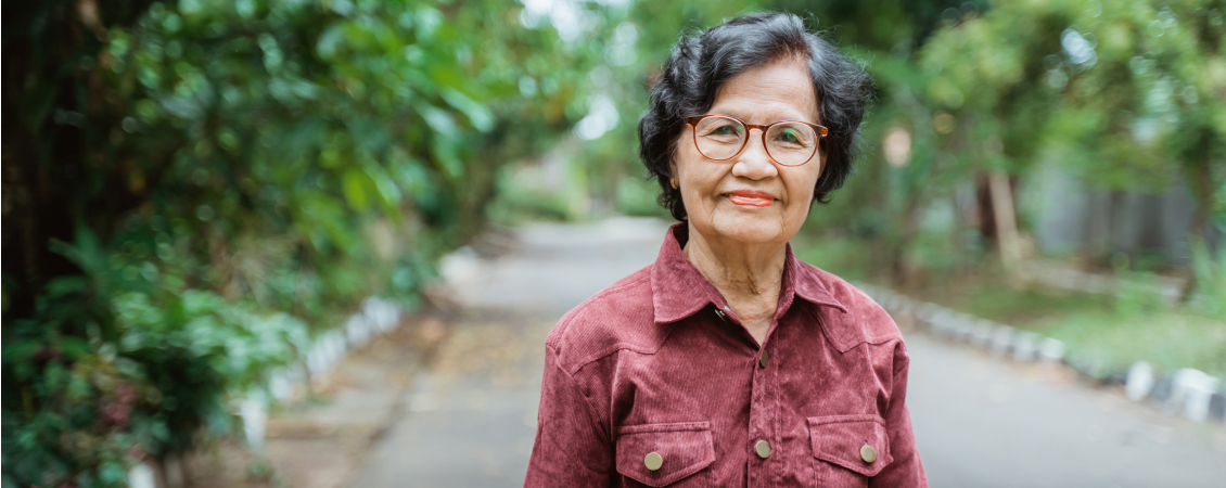 Asian woman wearing glasses standing on a tree-lined street.