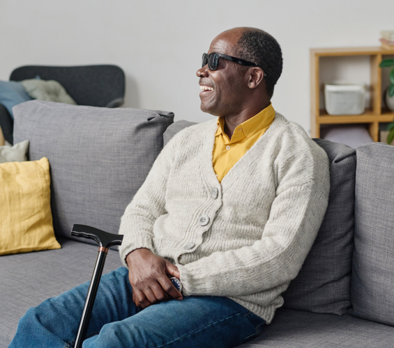 Man sitting on couch with dark shades and a cane.