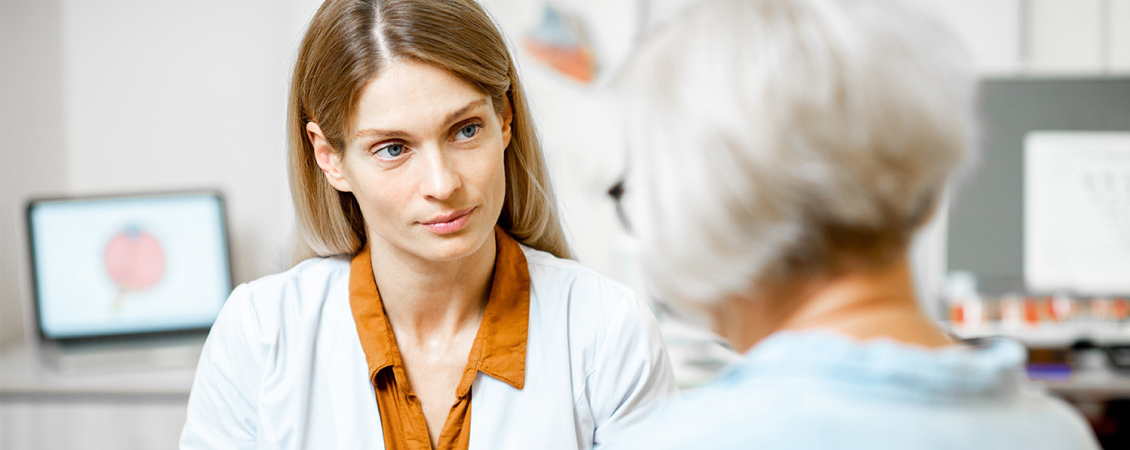 Female doctor in white labcoat speaking with elderly woman patient.