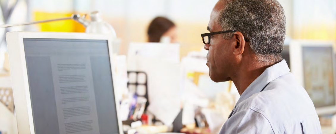 A man uses a computer while sitting at a desk.