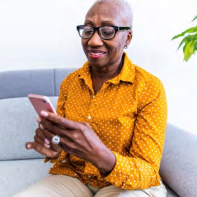 A woman wearing a yellow shirt uses a smart phone while seated on a couch.